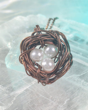 Necklace with a bird's nest pendant and pearls on a textured surface