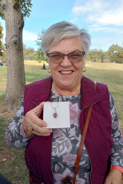 Woman holding a necklace with a purple pendant outdoors
